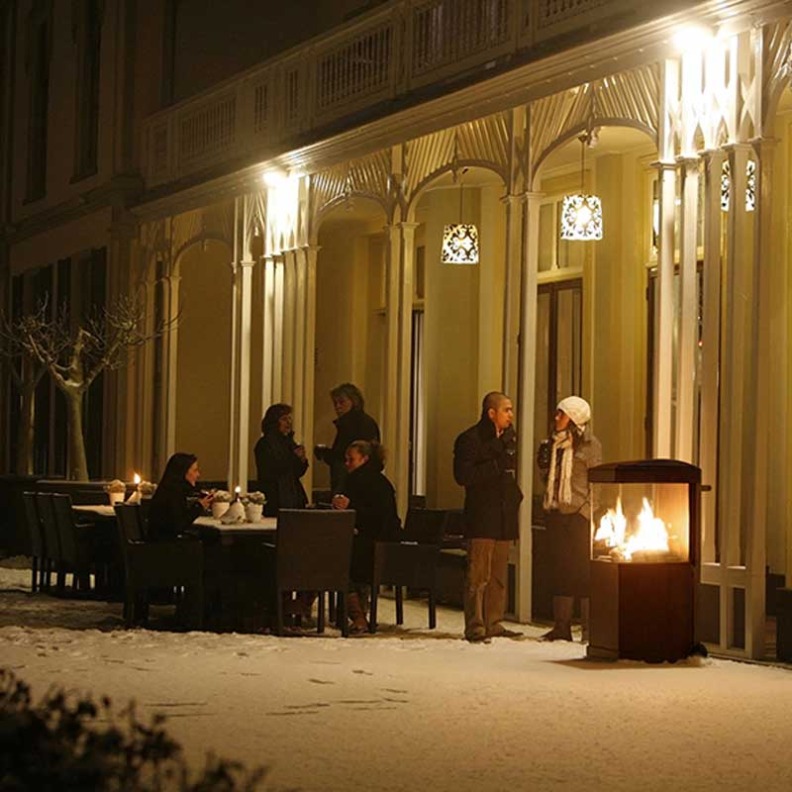 Cheminée à gaz The Buzz de Faber installée de nuit sur une terasse en extérieur sous les éclairages