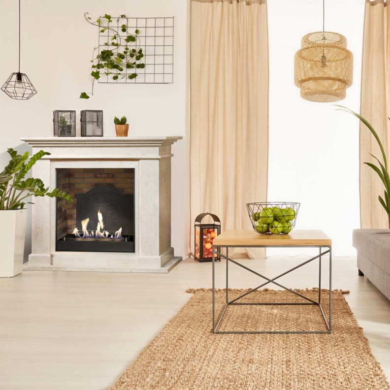 Cheminée Xaralyn Kos en parements de pierre crème au bioéthanol avec un fond brique et fausse plaque de fonte